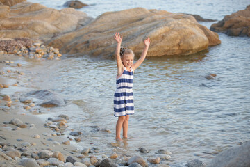 Cute little girl in blue and white striped dress on the wild empty beach