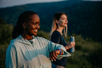Active Lifestyle in the Wilderness: Embracing an active lifestyle, black and white female joggers navigates a trail in a lush forest, using their smartwatch to maintain their pace and monitor their ov