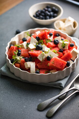 Summer salad with watermelon, feta cheese and blueberry on a gray background. Vegan, European food.