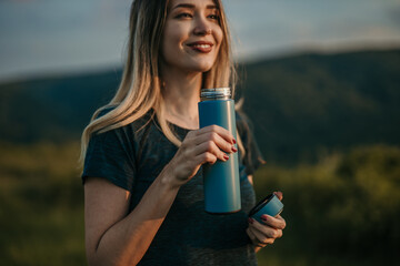 Woman staying hydrated: Capture the essence of a woman in a sports outfit outdoors in nature as she...