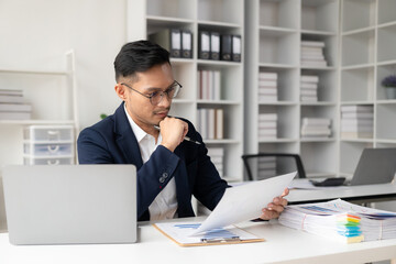 Asian businessman writing financial graph chart marketing information plan Male hand using laptop at desk reading financial document spreadsheet for calculation and analysis.