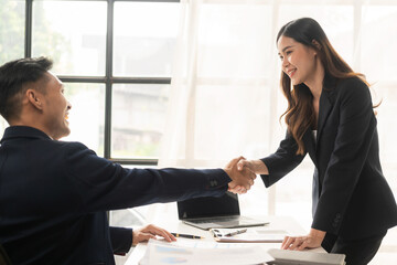 Happy young asian business man and woman shaking hands to congratulate successful collaboration on business deal with documents and laptop on table - obrazy, fototapety, plakaty