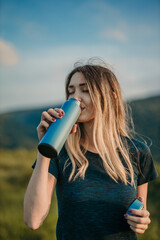 Fitness motivation: Depict a woman drinking water in a sports outfit amidst breathtaking natural surroundings, inspiring viewers to engage in physical activities and prioritize their well-being.