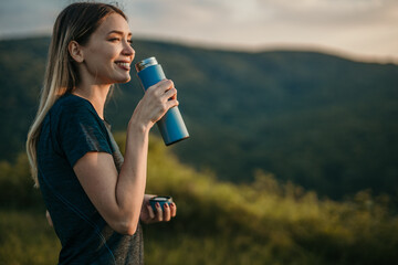 Fitness motivation: Depict a woman drinking water in a sports outfit amidst breathtaking natural surroundings, inspiring viewers to engage in physical activities and prioritize their well-being.
