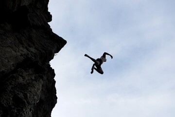 Silhouette of man jumping off cliff.