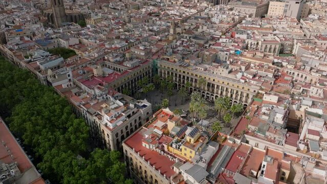 Aerial slide and pan shot of dense town development in urban borough. Green vegetation of La Rambla street and Placa Reial square. Barcelona, Spain