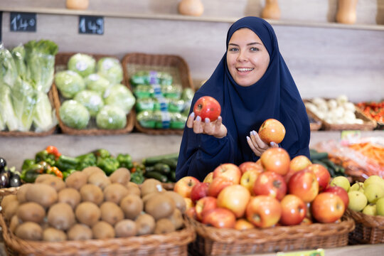 Girl in paranja making purchases in supermarket, choosing fresh ripe apples
