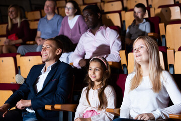 Cheerful parents with tween daughter watching stage performance in theater. Family leisure and...