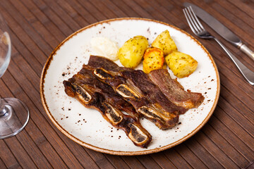 Service plate containing grilled steak and slices of potato with necessary table laying