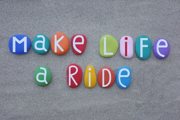 Make life a ride, creative slogan composed with multi colored stone letters over green sand
