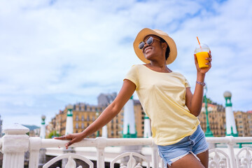 Black ethnic woman having an orange juice enjoying the summer in the city