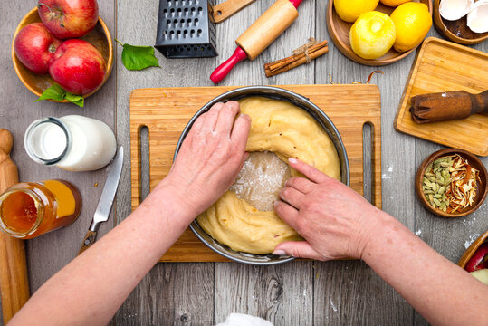 Hands Of The Cook And The Kitchen Table In The Process Of Preparing An Apple Pie. Flour, Rolling Pin, Milk, Apples, Eggs And Kitchen Utensils On A Gray Table. View From Above.