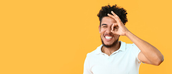 Portrait of happy African-American man showing OK gesture on yellow background with space for text