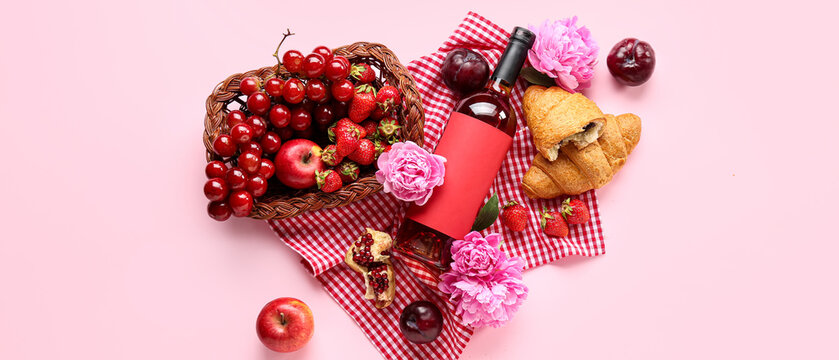 Tasty food for picnic with wine and peony flowers on pink background, top view