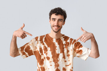 Handsome man pointing at tie-dye t-shirt on light background