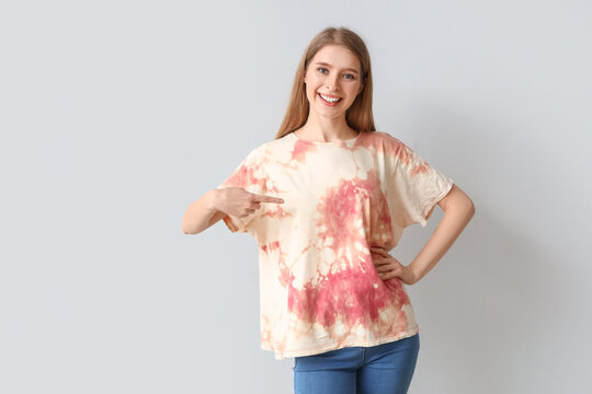 Young woman pointing at tie-dye t-shirt on light background