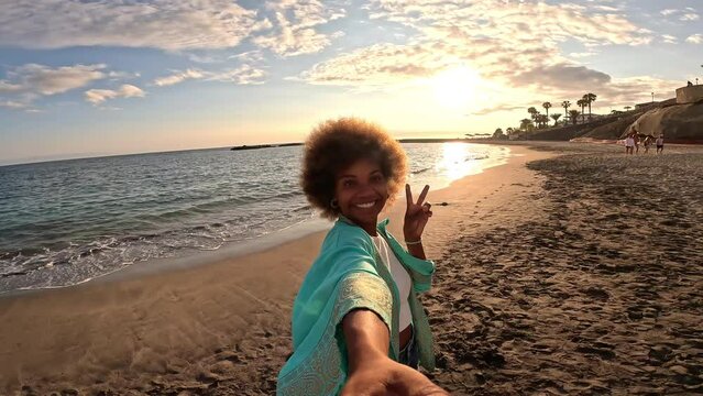 One afro multiracial young beautiful woman holding and looking at the camera taking a selfie at the beach enjoying summer time outdoor on holiday. 

