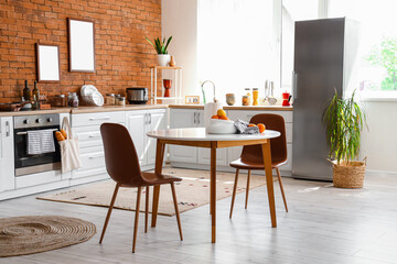 Fototapeta na wymiar Interior of kitchen with stylish fridge, counters, table and chairs