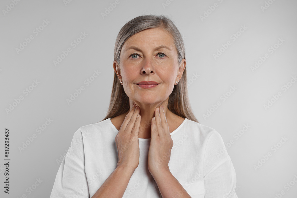 Wall mural Endocrine system. Senior woman doing thyroid self examination on light grey background