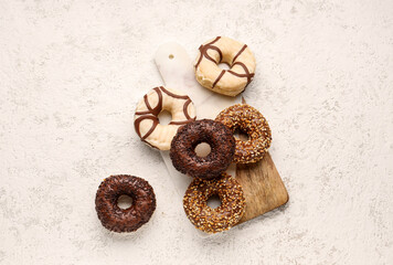 Fototapeta na wymiar Board with sweet chocolate donuts on light grunge background