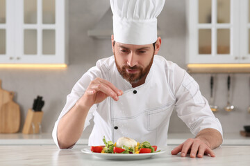 Professional chef salting delicious salad at marble table in kitchen