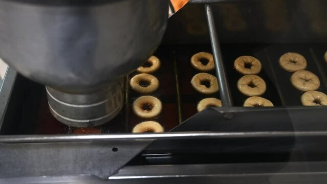 The machine forms and fries mini donuts in oil. Cooking mini donuts in production on an automated conveyor line. Preparing fresh baked goods. Step 1.