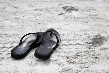 black flip flops on sand, calm soothing sand beach background with copy space