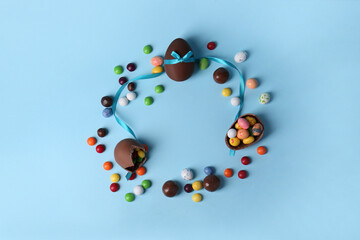 Frame made of tasty chocolate eggs and different candies on light blue background, flat lay with space for text