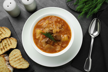 Tasty cabbage soup with meat, carrot and dill served on black table, flat lay