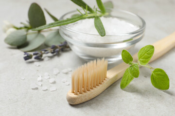 Bamboo toothbrush, sea salt and herbs on light grey table, closeup