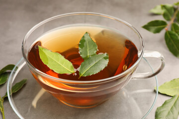 Cup of freshly brewed tea with bay leaves on grey table, closeup