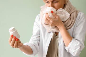 Ill mature woman with tissues and pill bottle on green background, closeup