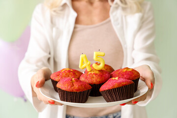 Mature woman with birthday muffins on green background, closeup