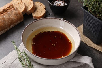 Bowl of balsamic vinegar with oil, spices and bread on dark grey table