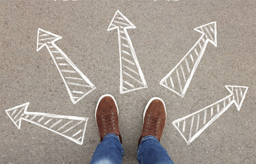 Choosing future profession. Man standing in front of drawn signs on asphalt, top view. Arrows...