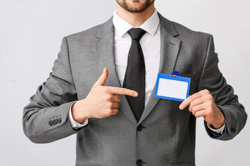 Young businessman pointing at blank badge on light background