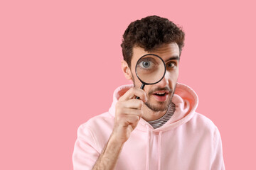 Young man with magnifier on pink background, closeup