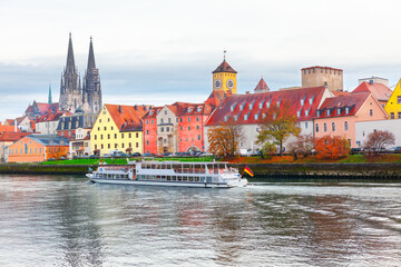 Fototapeta premium Regensburg city on a river in Bavaria , Germany . Tourist boat on the Danube river in Regensburg . Clock tower and cathedral at riverside in autumn 