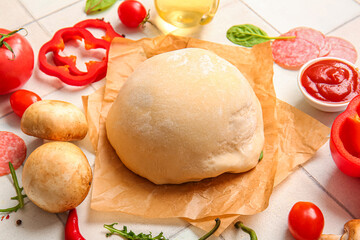 Raw dough and ingredients for preparing pizza on white tile background