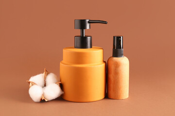 Bottles of cosmetic products and cotton flower on color background
