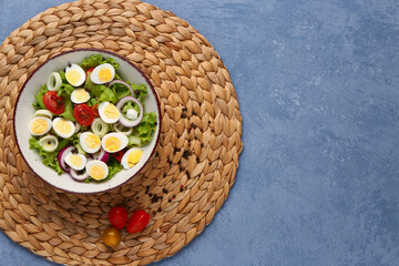 Tasty salad with quail eggs, tomatoes, onion and lettuce on blue background