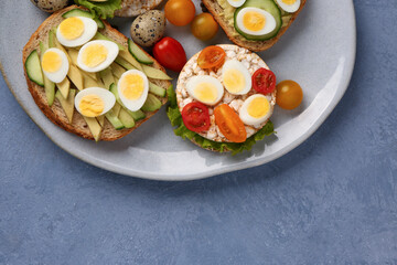 Fototapeta na wymiar Different tasty toasts with quail eggs, avocado and tomatoes in plate on blue background