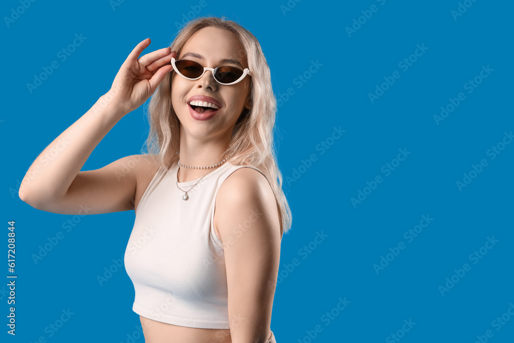 Wall mural young woman in stylish sunglasses on blue background