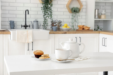 Fototapeta na wymiar Interior of light kitchen with teapot, cup and snacks on table
