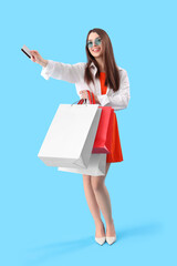 Young woman with gift card and shopping bags on blue background