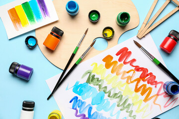 Composition with different paints, brushes and rainbow color palette on blue background