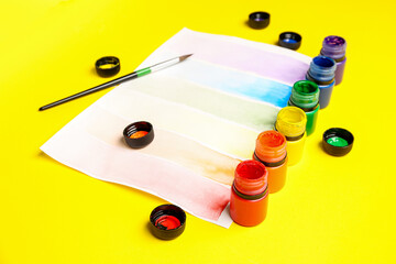 Composition with different paints, brush and rainbow color palette on yellow background