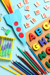 Color paper rocket with abacus, wooden letters and pencils on color background