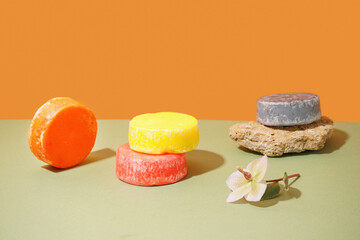 Solid colorful shampoo bars with stone and flower on green table orange wall