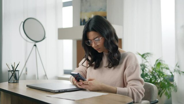 Concerned young elegant successful beautiful hispanic business woman. Professional startup entrepreneur executive holding cellphone using smartphone modern tech working remotely in modern apartment 4K